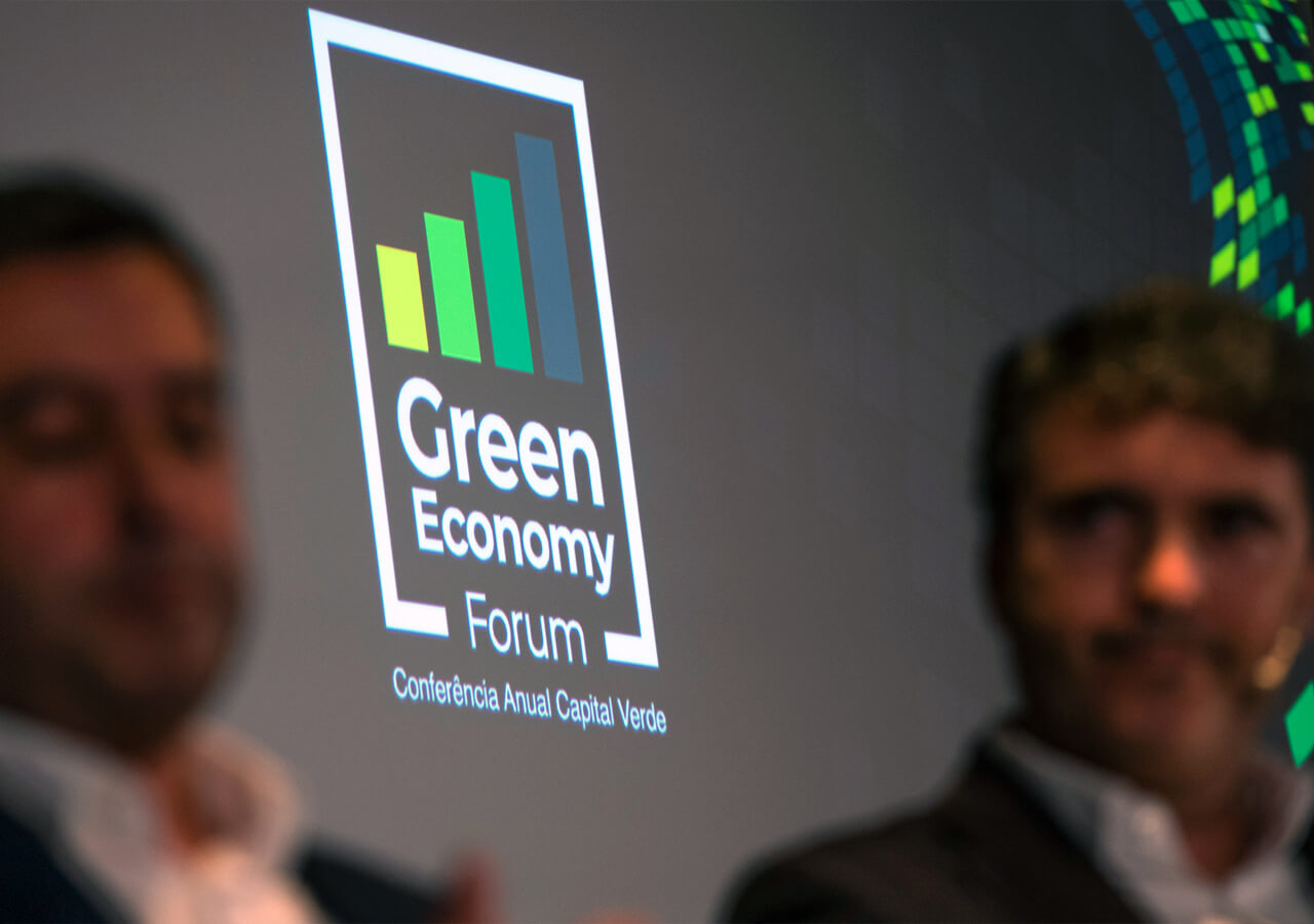 imagem do logotipo do green economy forum 2022, projetada no palco, com dois oradores desfocados em primeiro plano